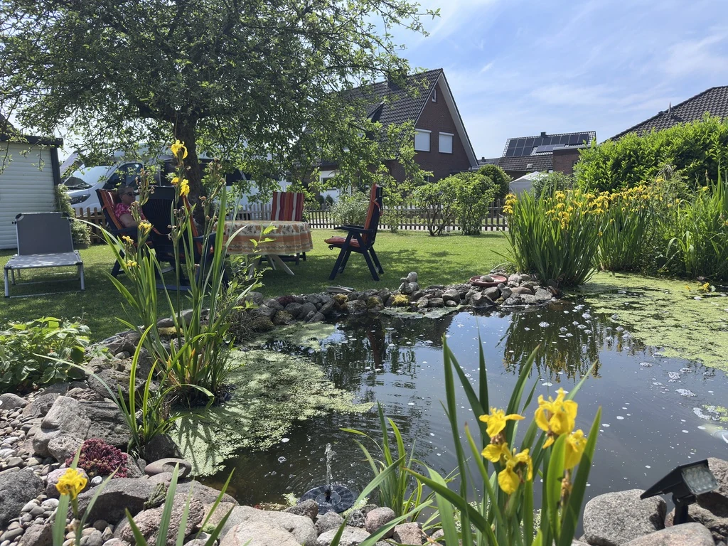 Unser Gartenteich mit gelben Wasserpflanzen und Sitzplatz im Garten